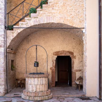 Cortile rustico con pozzo e scale in pietra.