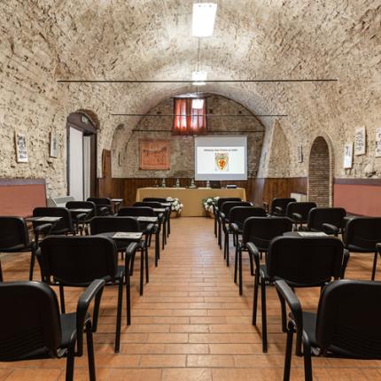 Sala conferenze in pietra con sedie e proiettore.