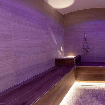 Stanza relax con luci soffuse viola e sedute in legno.