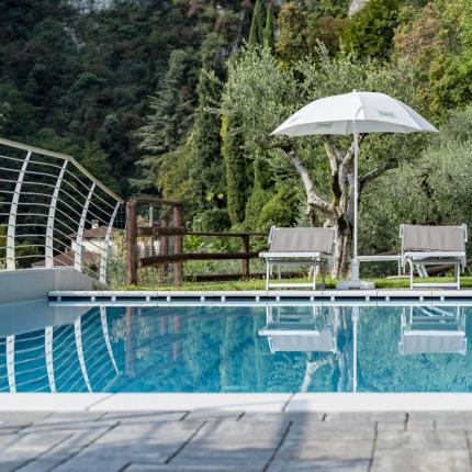 Piscina tranquilla con ombrellone, sedie e natura rigogliosa intorno.