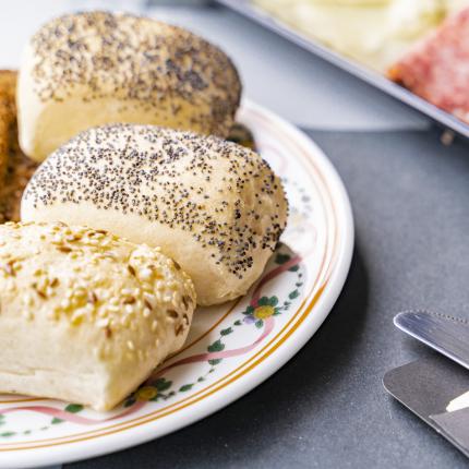 Panini fragranti con semi, salumi e posate eleganti su tavola raffinata.