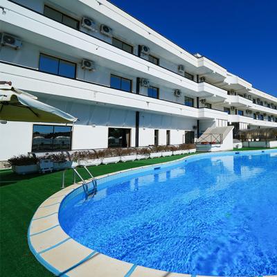 Hotel moderno con piscina e giardino, cielo blu limpido.