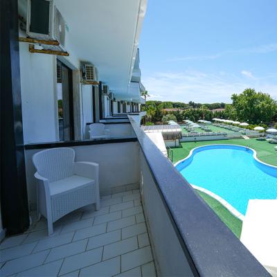 Balcone con vista piscina e lettini in un hotel soleggiato.