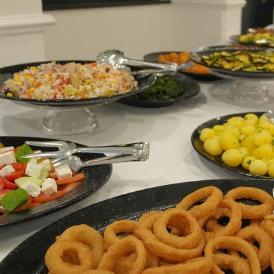 Buffet con anelli di cipolla e insalate varie su piatti neri.