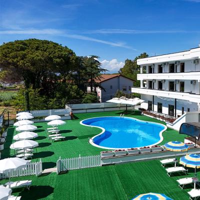 Hotel con piscina all'aperto, ombrelloni e sdraio su prato verde.