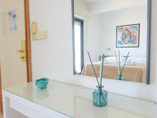 Bright room, mirror reflects cozy bed and colorful art.