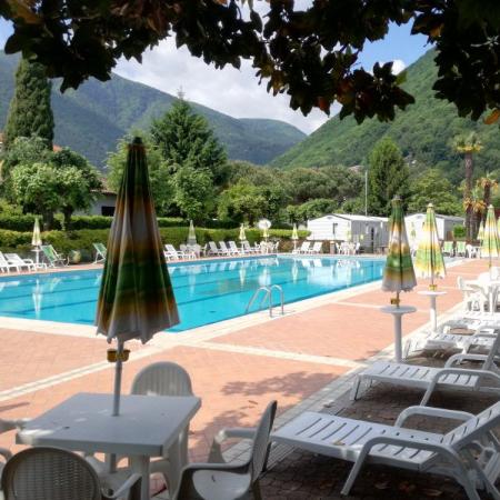 Piscina all'aperto con lettini e ombrelloni, circondata da montagne verdi.