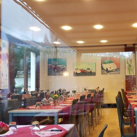 Ristorante elegante con tavoli apparecchiati e quadri di auto.