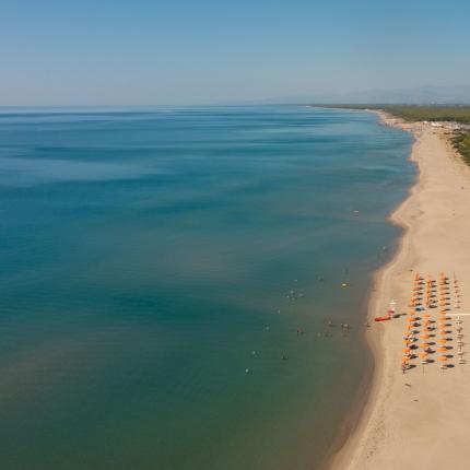 Spiaggia sabbiosa con ombrelloni arancioni e mare calmo.