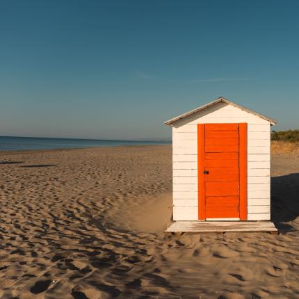 Casetta bianca con porta arancione su una spiaggia deserta.