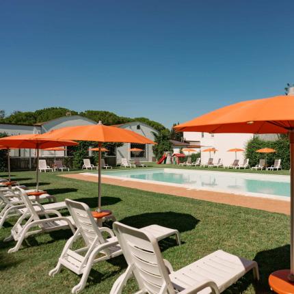 Piscina all'aperto con ombrelloni arancioni e sdraio bianche su prato verde.