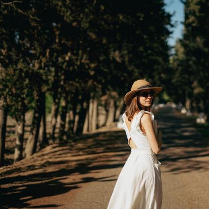 Donna con cappello cammina su un sentiero alberato.