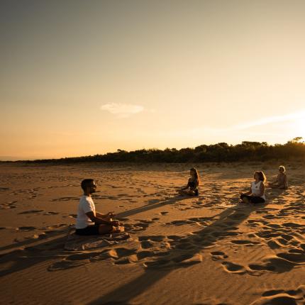 Gruppo medita al tramonto su una spiaggia sabbiosa.