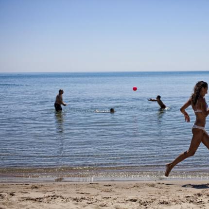 Donna corre sulla spiaggia, persone giocano in acqua.