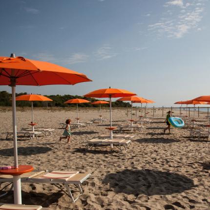 Spiaggia con ombrelloni arancioni e lettini, cielo sereno.