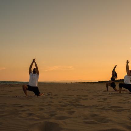 Persone fanno yoga sulla spiaggia al tramonto.