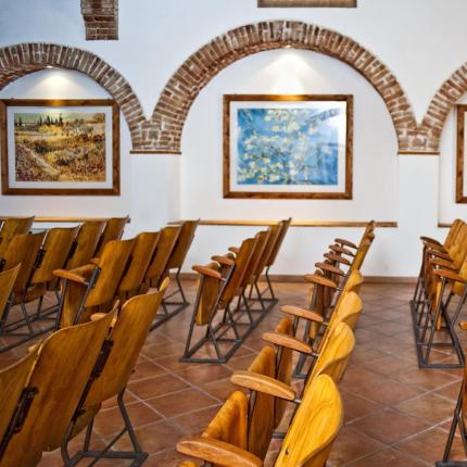 Sala conferenze con sedie di legno e dipinti alle pareti.