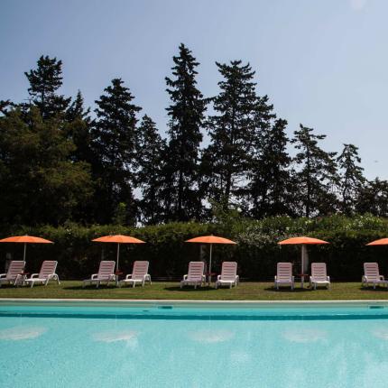 Piscina con lettini e ombrelloni arancioni, circondata da alberi.