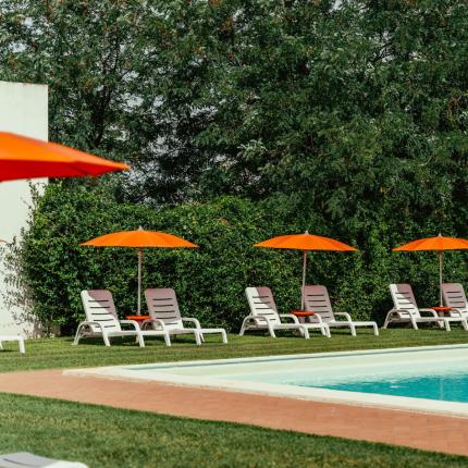 Piscina con lettini e ombrelloni arancioni, circondata da alberi.