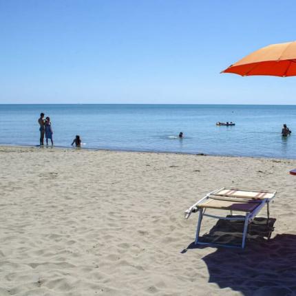 Spiaggia sabbiosa con ombrellone arancione e sdraio, mare calmo.