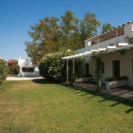 Casa bianca con pergolato e giardino, cielo sereno.