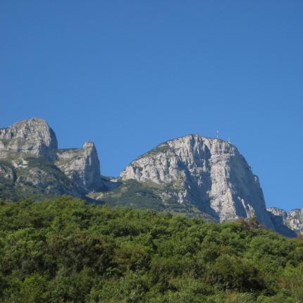 Montagna rocciosa con cielo azzurro e vegetazione verde.