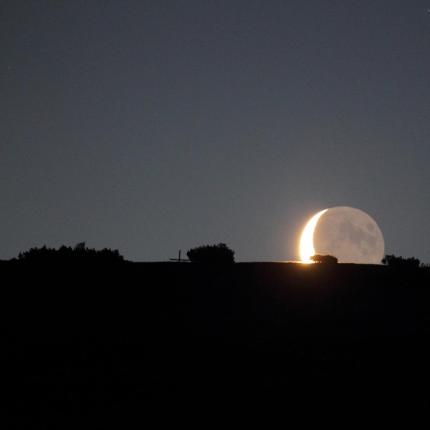 La luna crescente sorge dietro l'orizzonte notturno.