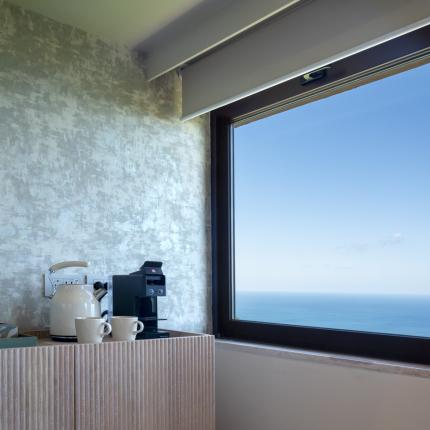 Sea view from a modern kitchen with coffee maker and mugs.