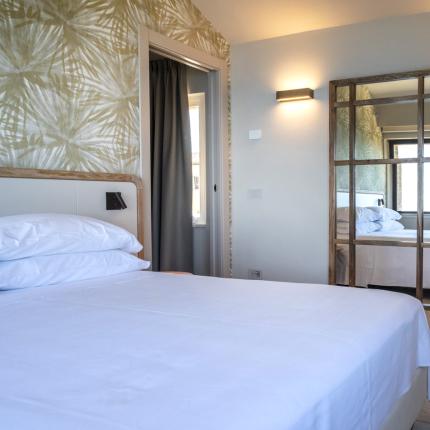 Cozy room with white bed and mirror, serene and bright atmosphere.