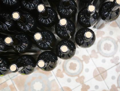 Bottiglie di vino scuro su piastrelle colorate, evocano eleganza e tradizione.