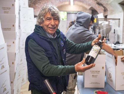 Uomo sorridente mostra una bottiglia di vino in cantina vivace.