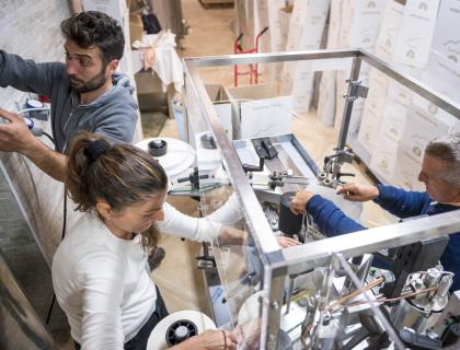 Tre persone lavorano insieme su una macchina in un magazzino pieno di scatole.