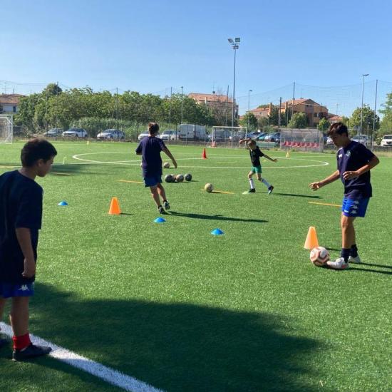 Giovani calciatori si allenano sul campo con coni e palloni.