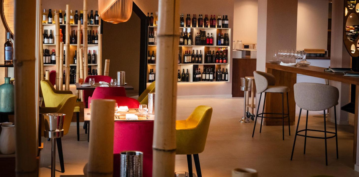 Ristorante elegante con luci soffuse, sedie colorate e scaffali pieni di bottiglie di vino.
