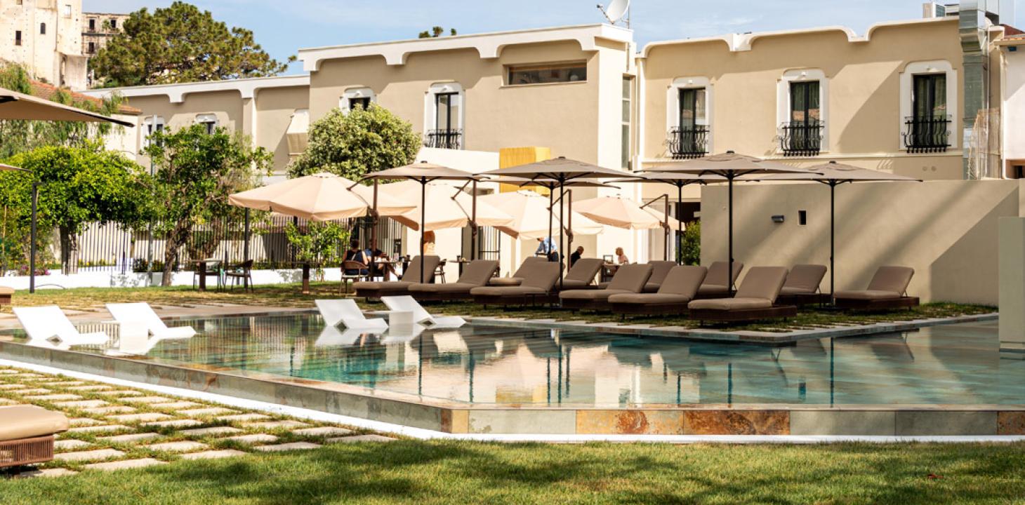 Piscina tranquilla con lettini e ombrelloni, circondata da edifici eleganti.