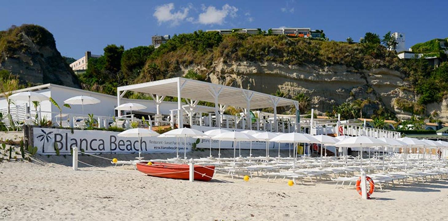 Spiaggia con ombrelloni bianchi e ristorante vista mare.