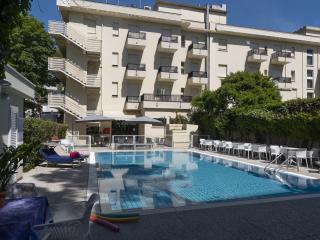 Heller Pool umgeben von weißen Stühlen, Sonnenschirmen und einem modernen Gebäude.