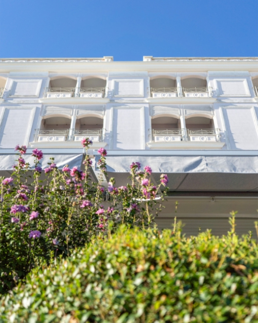 Edificio bianco elegante con fiori viola sotto un cielo azzurro.