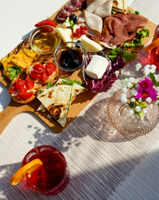 Tagliere colorato con salumi, formaggi, pane e cocktail estivi.