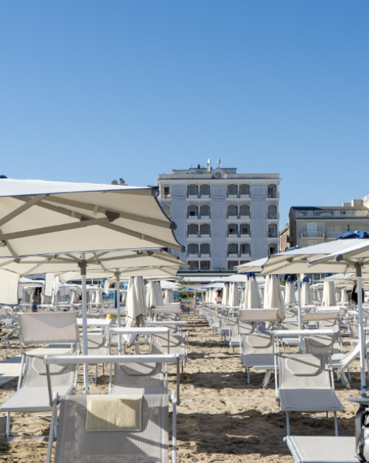 Spiaggia soleggiata con ombrelloni bianchi, atmosfera rilassante e cielo azzurro.