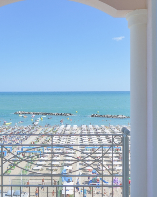 Vista sul mare azzurro e spiaggia affollata, sotto un cielo limpido.