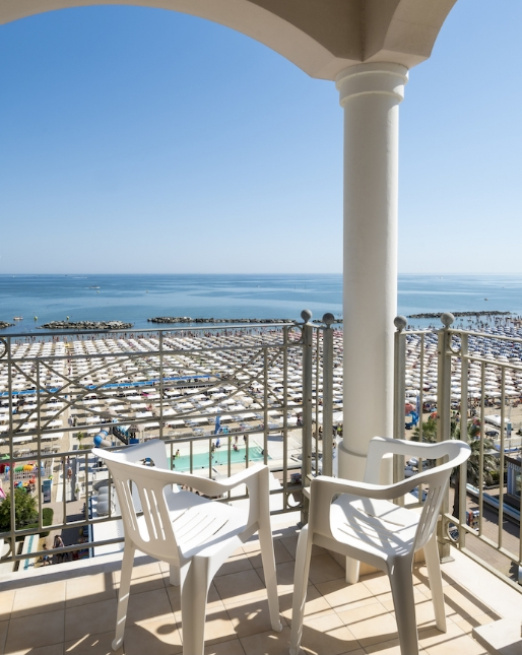 Vista mare con sedie bianche, sole e spiaggia affollata.