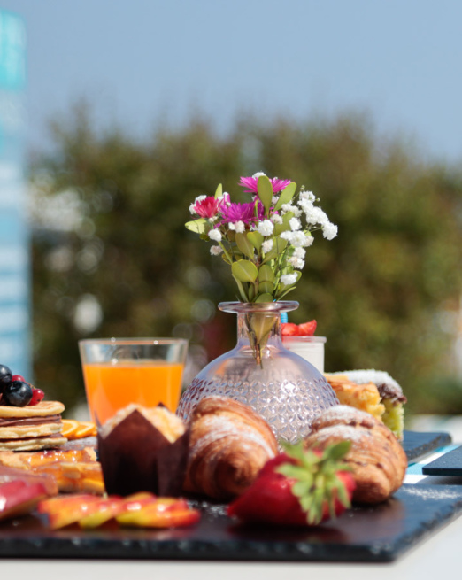 Colazione estiva all'aperto: fiori, dolci, succo e caffè con vista mare.