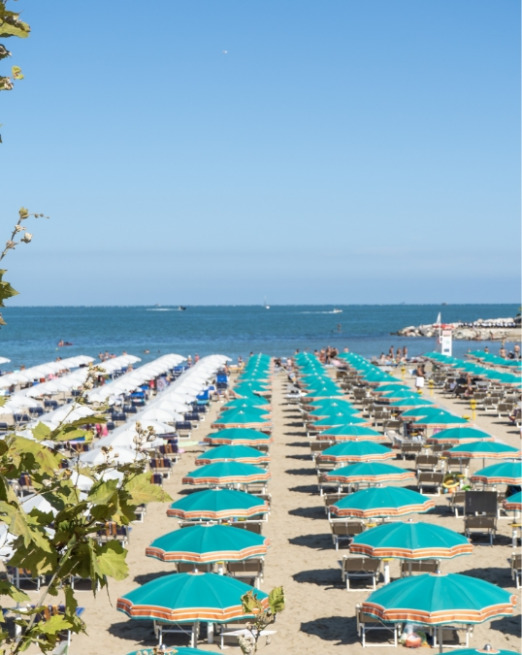 Spiaggia affollata di ombrelloni colorati sotto un cielo azzurro estivo.