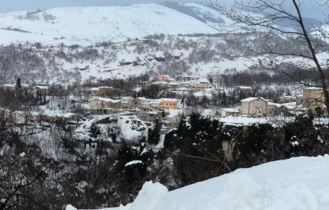 Paesaggio innevato con case e montagne sullo sfondo.