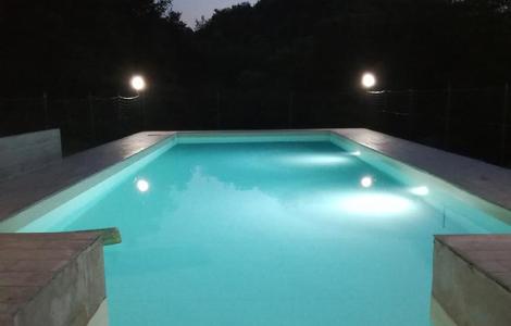 Piscina illuminata di notte con luci soffuse e cielo al crepuscolo.