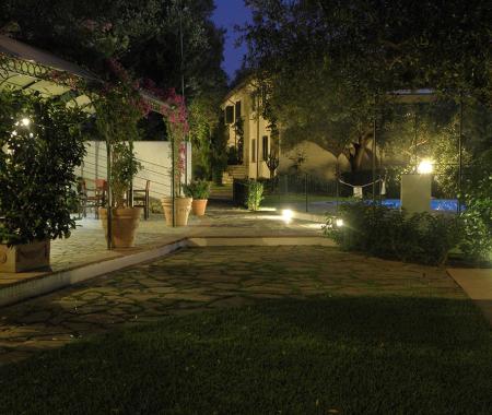 Giardino notturno con luci, tavoli e piscina.