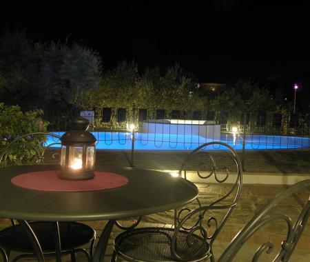 Piscina illuminata di notte con tavolo e lanterna.