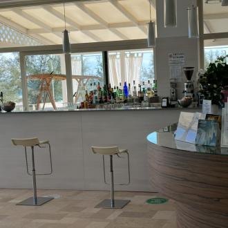 Moderno bar con bottiglie, sgabelli e cartelli informativi.