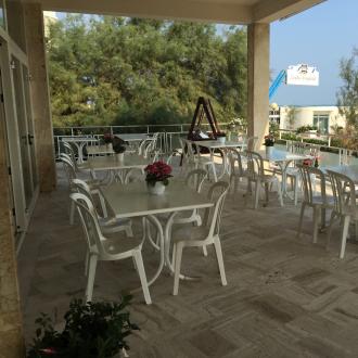 Terrazza con tavoli bianchi e sedie, vista mare.